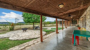 Eine überdachte Terrasse mit Steinboden, einem grünen Tisch und einem Grill.