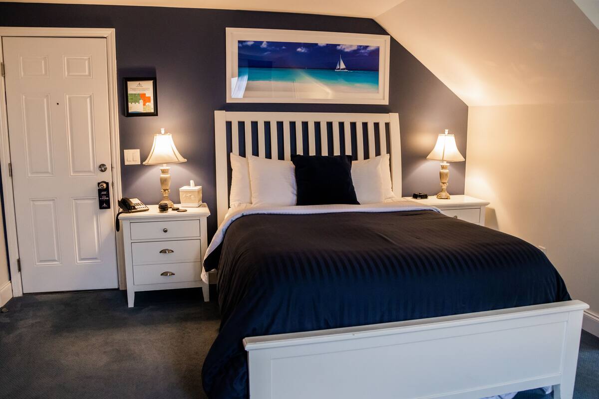 A bedroom with a bed, two bedside tables with lamps, a door, and a framed picture on the wall.