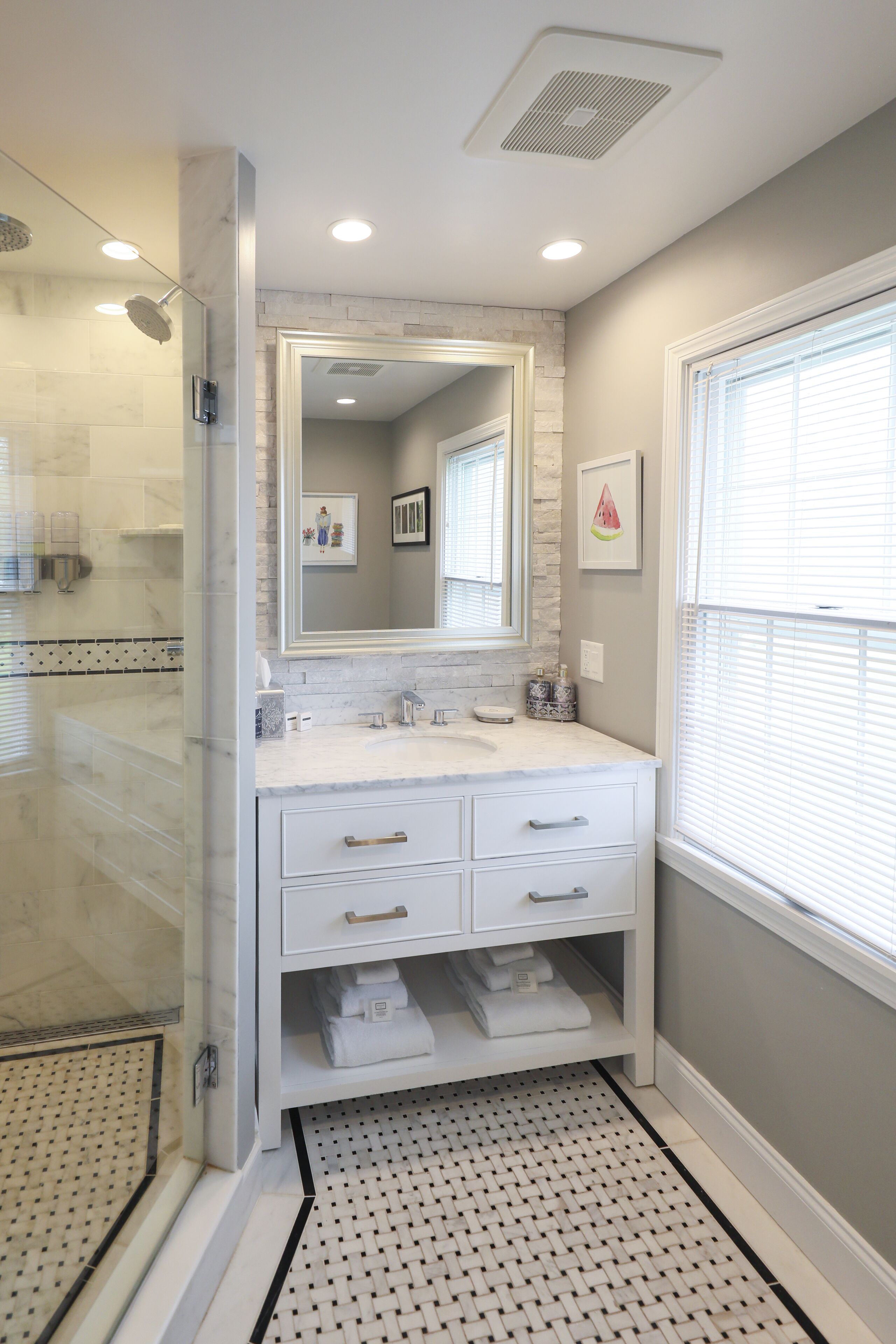 A bathroom with a glass-enclosed shower, a white vanity with drawers, a large mirror, and a tiled floor.