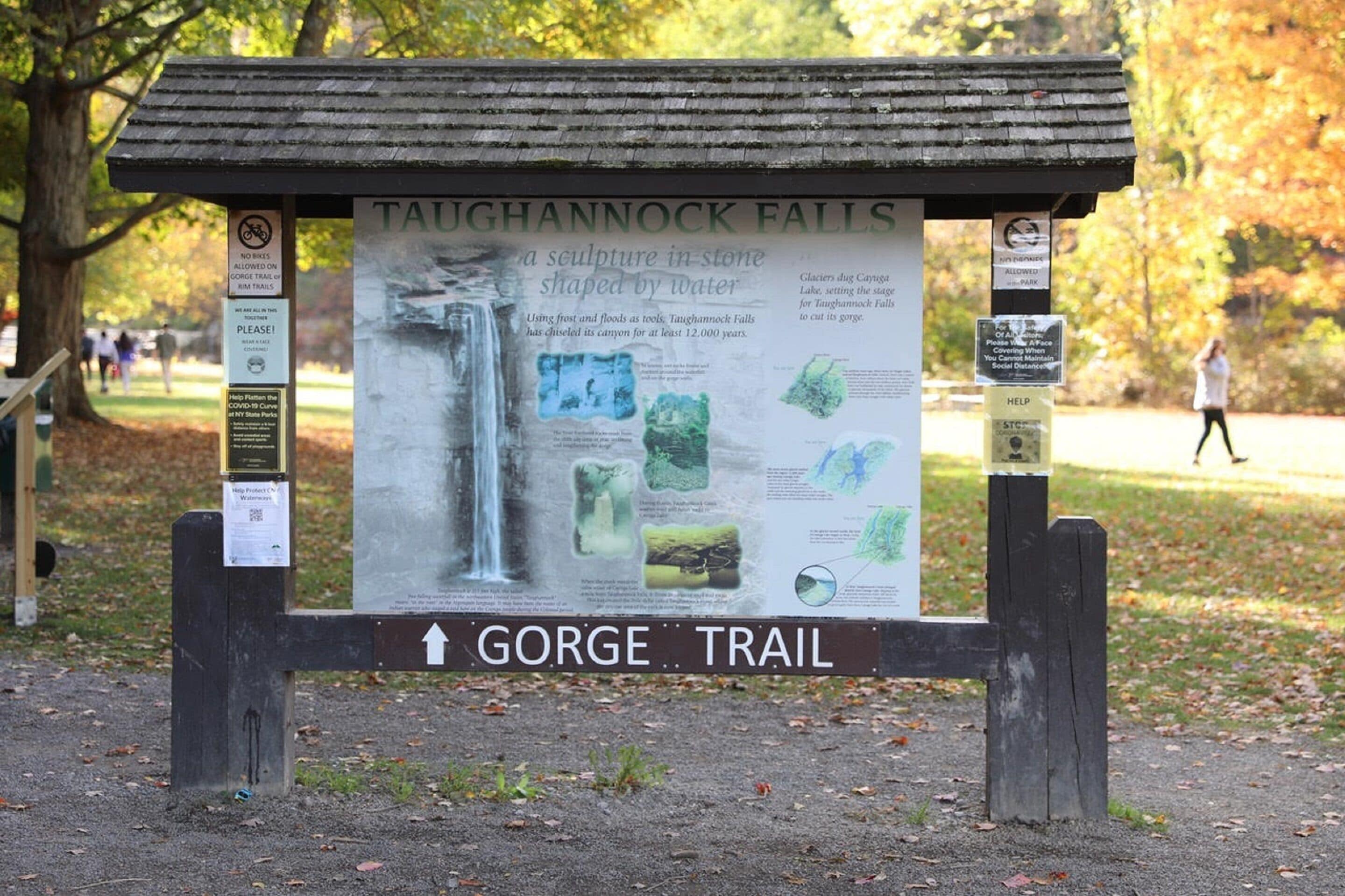 Un panneau d’information sur les chutes de Taughannock, une sculpture naturelle façonnée par l’eau, ainsi qu’un panneau indiquant le chemin menant au sentier de la gorge.