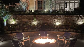 A house with a stone wall and a fire pit with chairs.