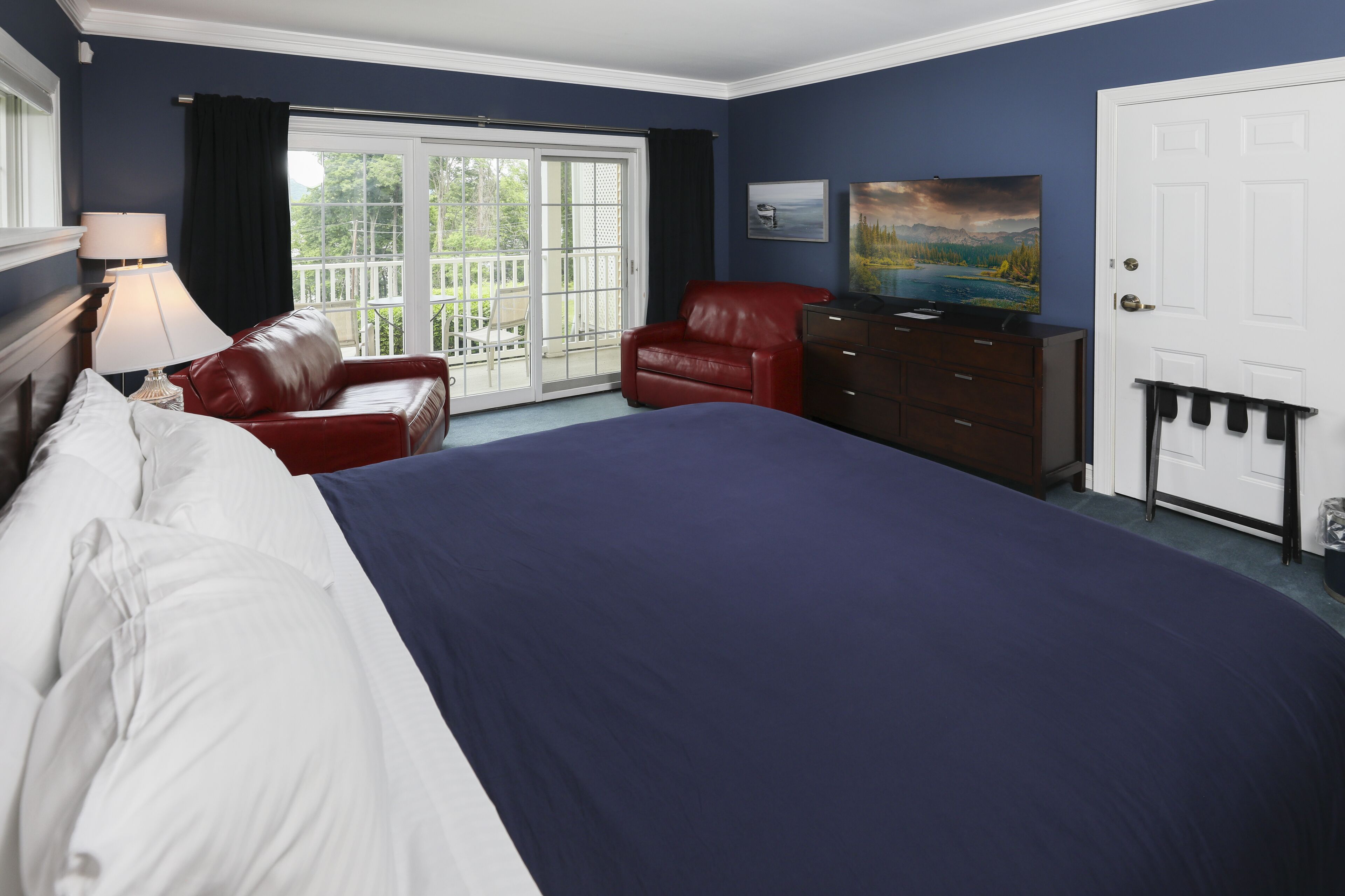 Een slaapkamer met een groot bed, een rode leren fauteuil, een dressoir en een schilderij aan de muur.