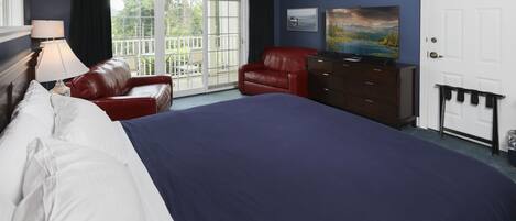 Een slaapkamer met een groot bed, een rode leren fauteuil, een dressoir en een schilderij aan de muur.
