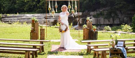 A wedding ceremony setup with wooden benches, a welcome sign, and hanging planters.