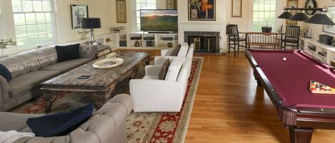 A spacious living room with a pool table, a comfortable sofa set, a fireplace, and a large TV.