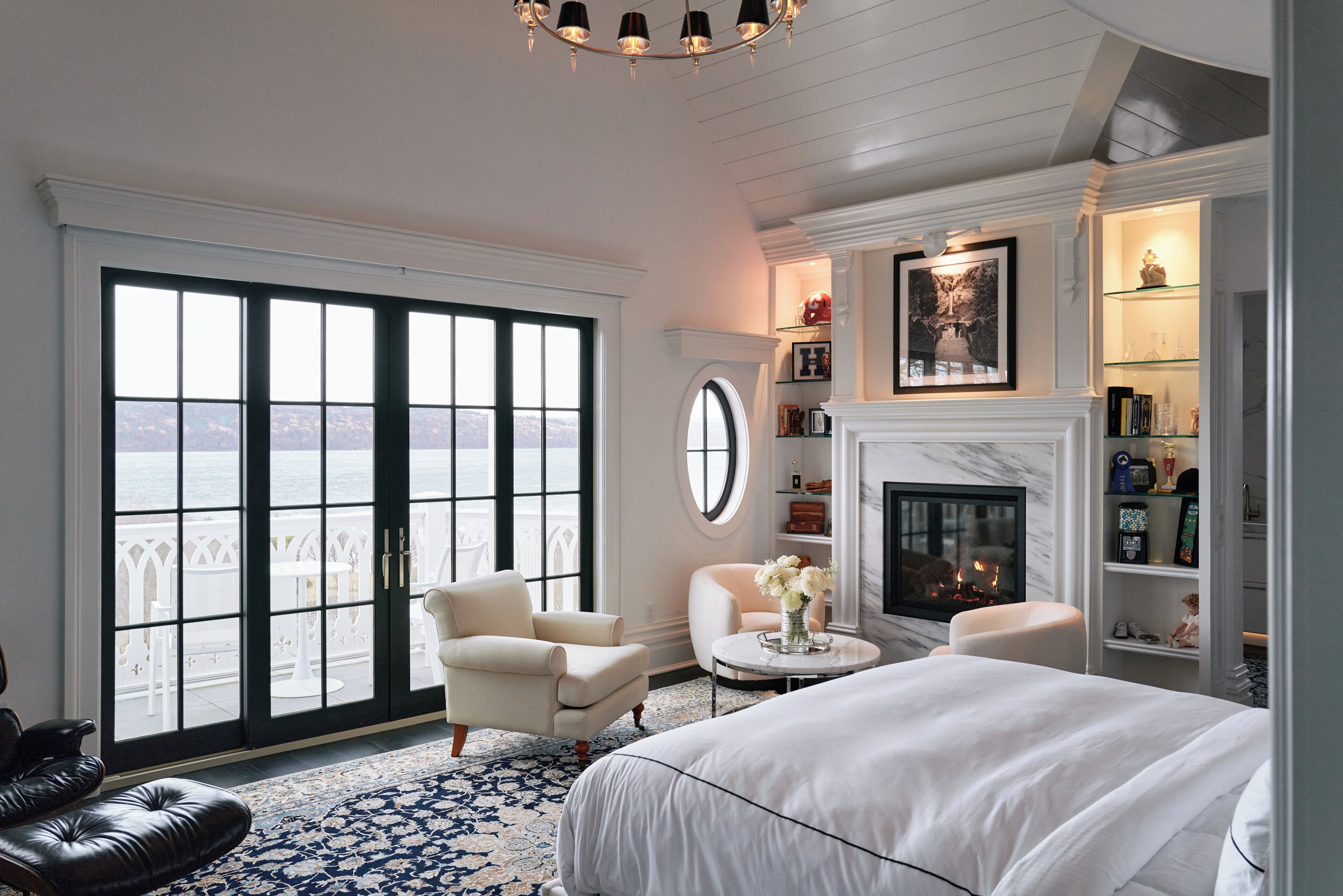 A bedroom with a large window, a fireplace, and a view of the sea.