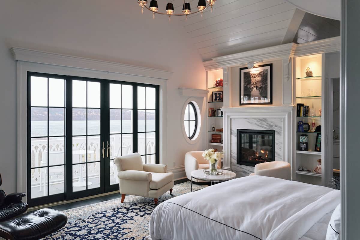 A bedroom with a large window, a fireplace, and a view of the sea.