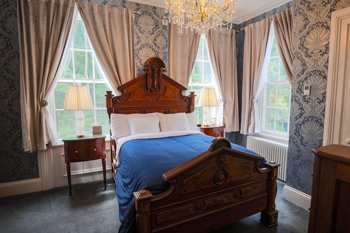 A bedroom with a wooden bed, two bedside tables, a chandelier, and patterned wallpaper.