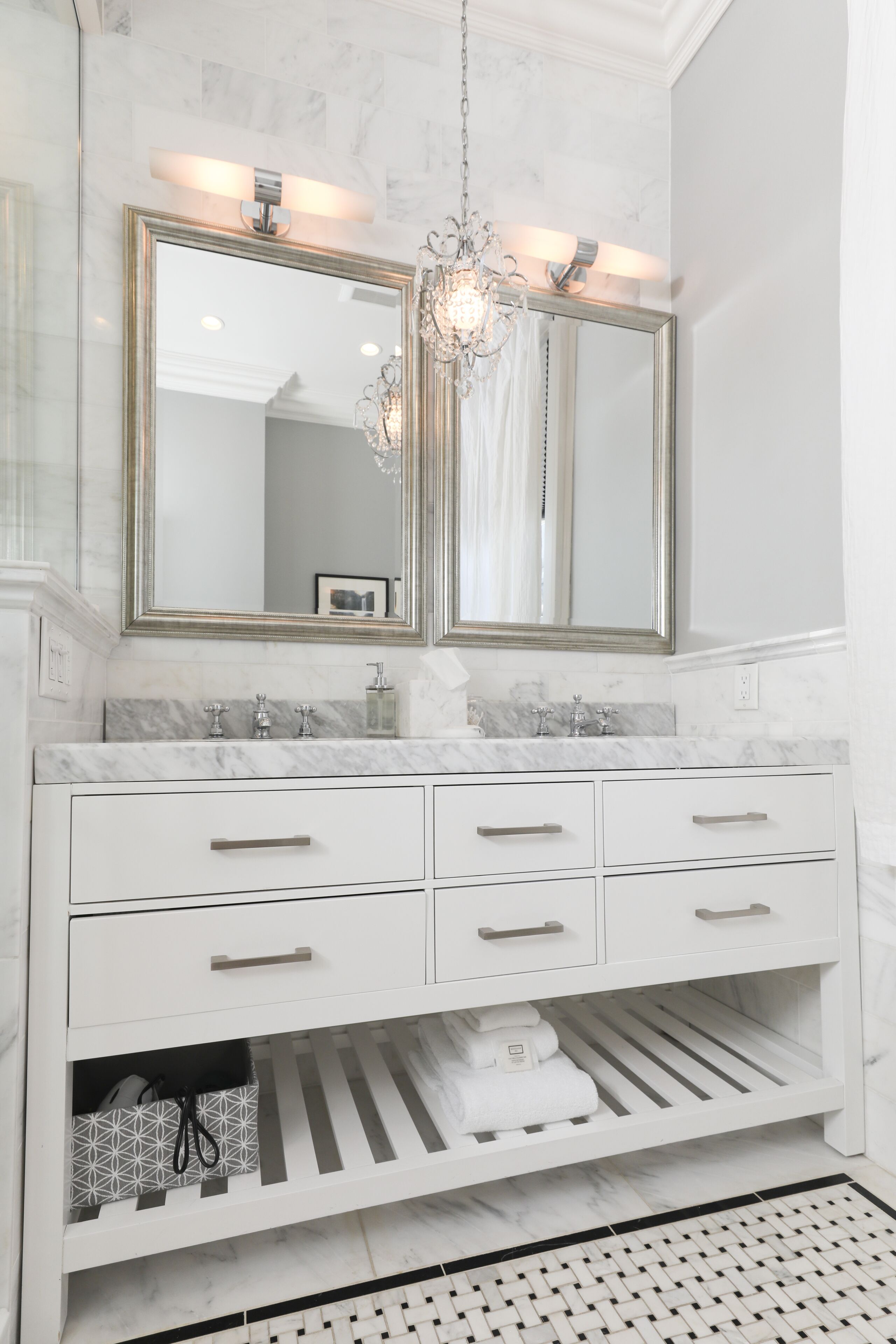 A bathroom with a double vanity, marble countertops, a chandelier, and a patterned floor.