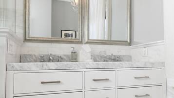 A bathroom with a double vanity, marble countertops, a chandelier, and a patterned floor.