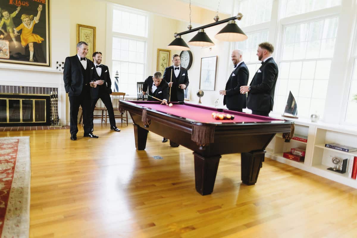 A billiards table in a room with wooden floors and large windows.