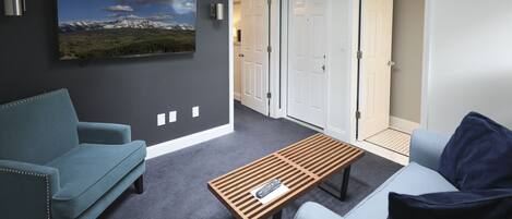 A modern living room with two sofas, a coffee table, and a mounted TV displaying a mountain landscape.