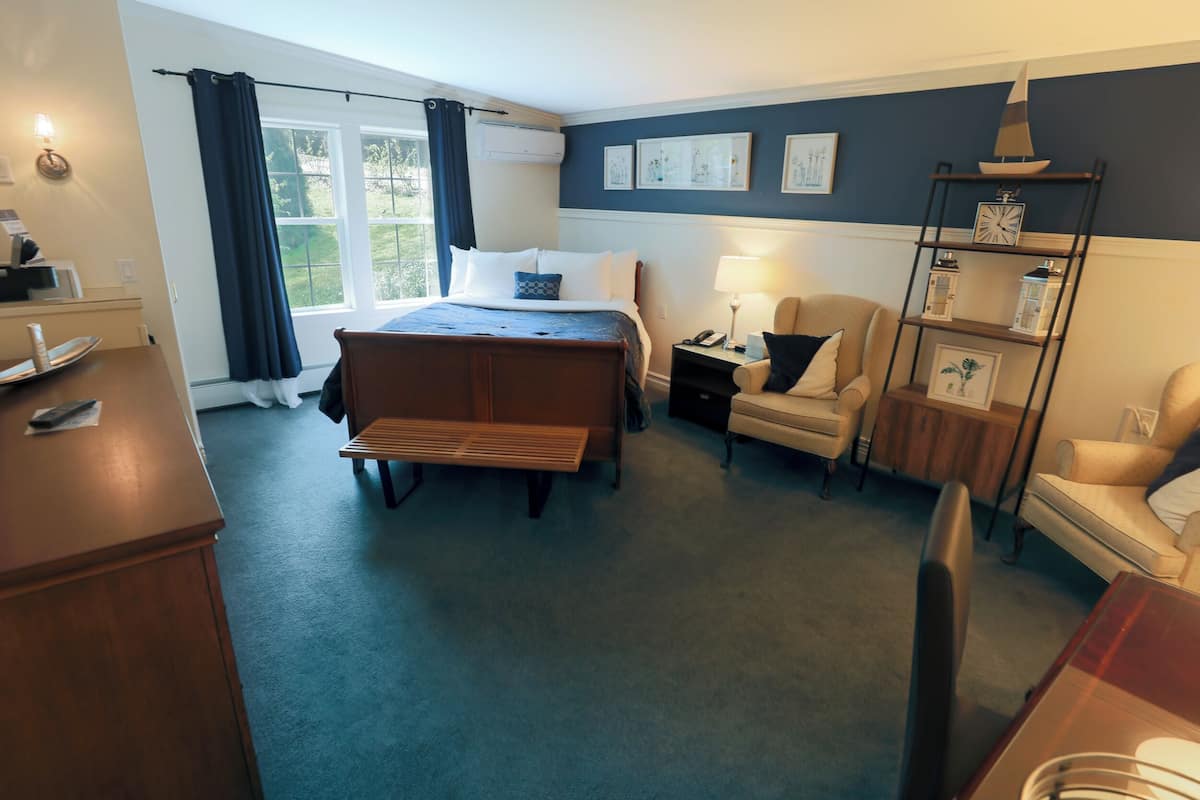 A hotel room with a bed, bedside tables, a desk, a chair, a bookshelf, and a window with curtains.