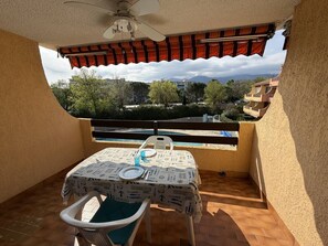 Un balcon avec une table dressée pour deux personnes, une chaise et une vue sur une piscine et des bâtiments.