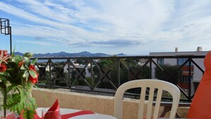 A table with a red tablecloth, white plates, and a glass of water, set on a balcony overlooking a coastal view with mountains in the distance. - 2P/Mezzanine Apt 4 Pers in Saint-Aygulf - Terrace, Parking, Washing Machine (Saint-Aygulf)