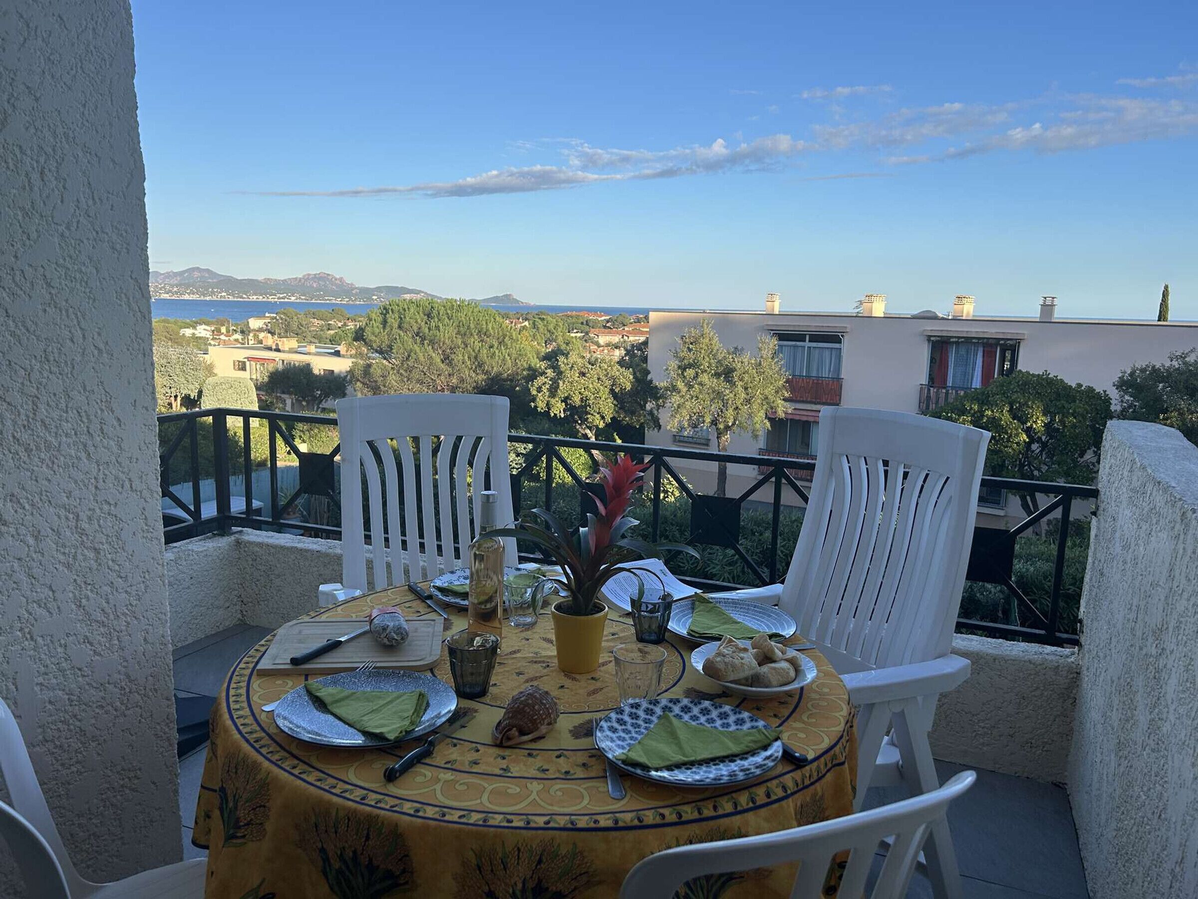 A round table with a yellow tablecloth, white chairs, and a view of a coastal landscape.