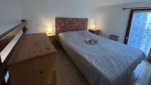A bedroom with a wooden bed frame, a bedside table with a lamp, a nightstand, and a window with a view. - 2P/Mezzanine Apt 4 Pers in Saint-Aygulf - Terrace, Parking, Washing Machine (Saint-Aygulf)