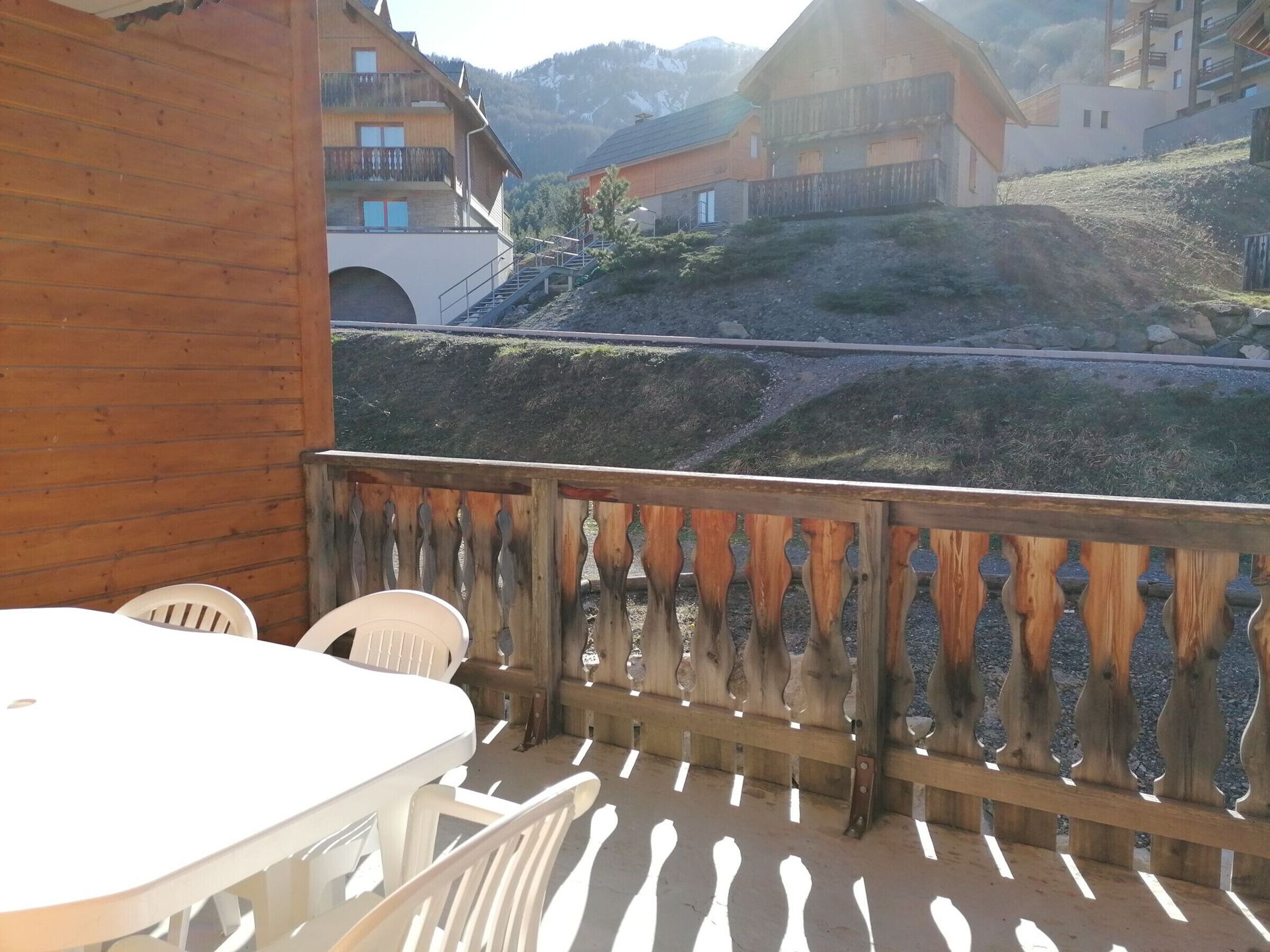 Un balcón de madera con una mesa y sillas, con vista a una zona montañosa con edificios tradicionales.