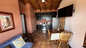 A cozy living room with a sofa, a dining table with chairs, a kitchen area with cabinets and appliances, and a ceiling fan.