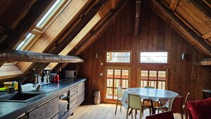 A cozy attic room with a wooden interior, a dining table, and a kitchen area with a sink and stove. - Charming 5-person mazot, renovated in Pra Loup, quiet hamlet (Pra-Loup)