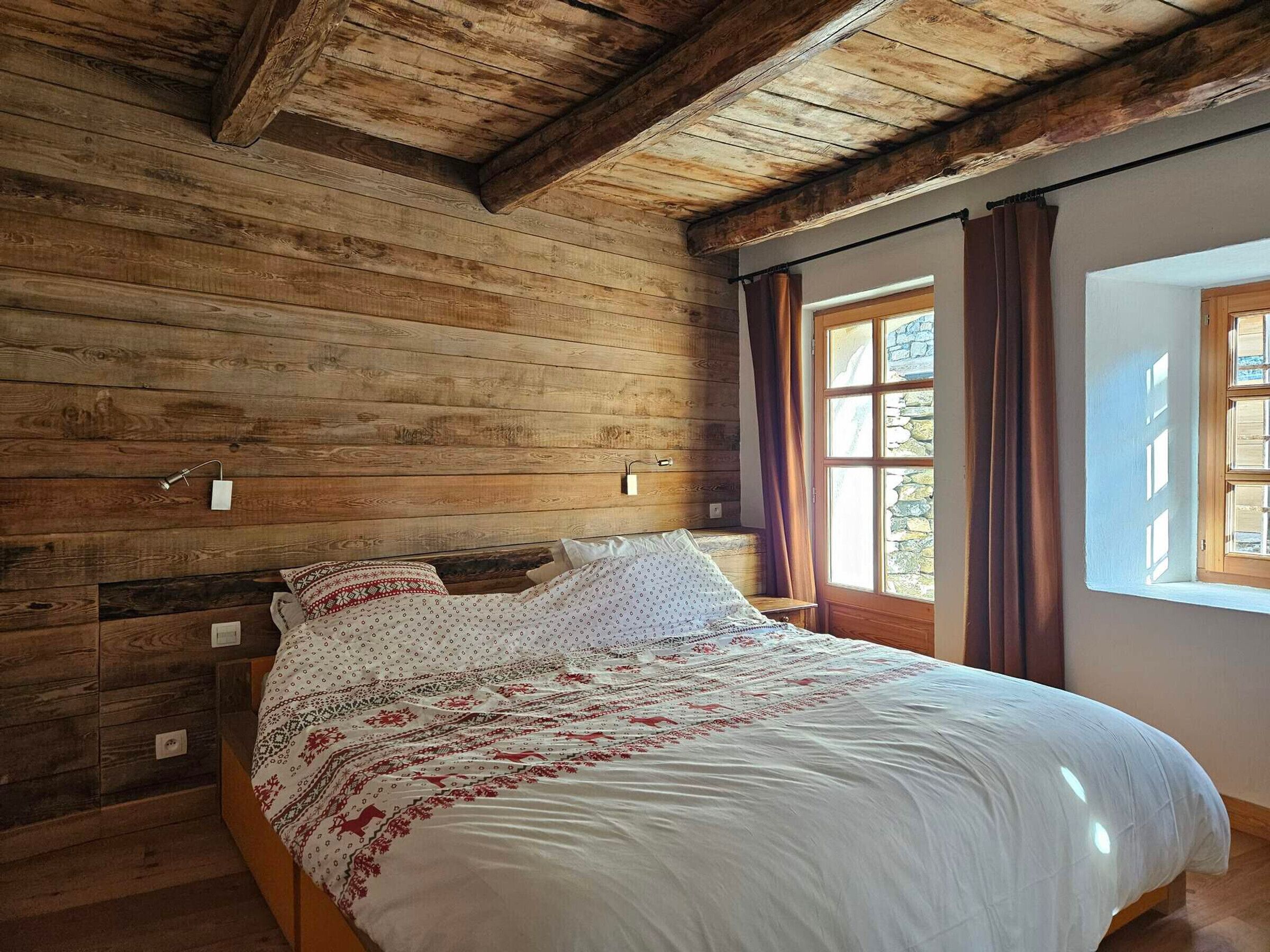 A wooden-paneled room with a bed, a window with curtains, and a wooden ceiling.