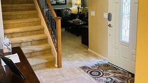 A staircase leading to a living room with a ceiling fan, a dining area with a table and chairs, and a patterned rug.
