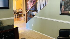A living room with a TV, a glass coffee table, a fireplace, and a staircase.
