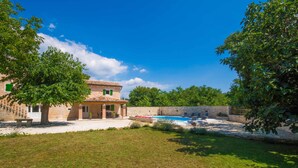 Una casa de dos pisos con piscina, rodeada de césped cuidado y árboles.