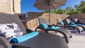 Sillones de exterior con cojines azules, un paraguas grande y una pared de piedra.