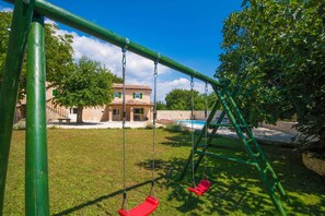 Ein Spielplatz mit Schaukeln und einem Schwimmbad im Hintergrund.