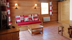 Una camera accogliente con pavimento in legno, un divano rosso, un tavolo in legno e due lampade a parete.