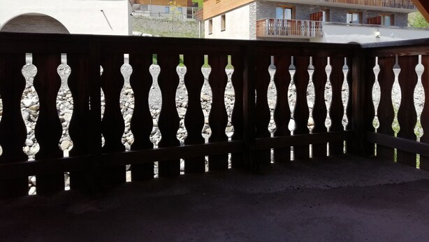 Un balcone in legno con balaustra in pietra che si affaccia su una zona montuosa con edifici.