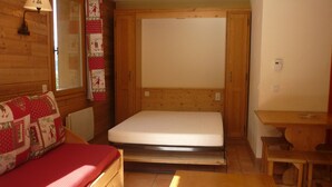 Un'accogliente stanza tipo baita con un letto di legno, un tavolino e una finestra vista aperta sulla natura.