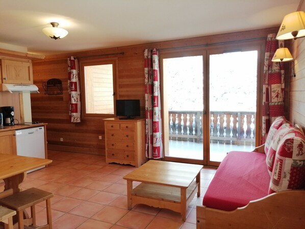 A cozy cabin-style room with wooden walls, a kitchenette, a dining area, and a balcony with a view.