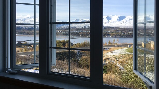 Une vue à travers une fenêtre à carreaux, donnant sur un paysage composé de montagnes, d’une rivière et d’un pont.