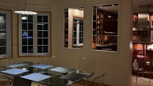 Un espace repas moderne avec une table et des chaises en verre, un lustre et une vue sur la cuisine.