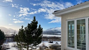 Une maison avec une grande fenêtre, un paysage enneigé et des montagnes en arrière-plan.