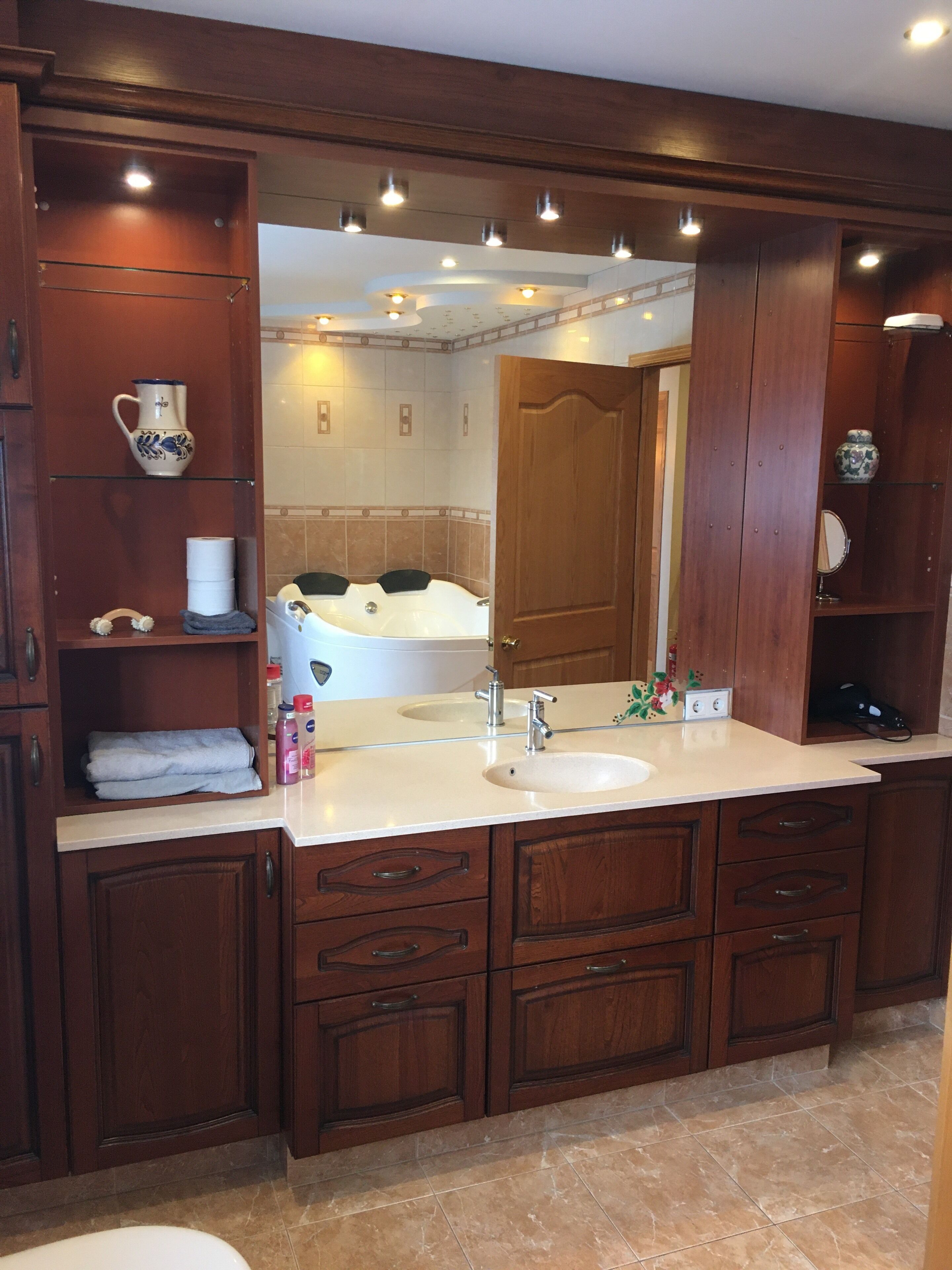 Un baño con lavamanos doble, armarios de madera, un espejo grande y una bañera.