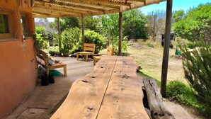 A wooden table under a wooden pergola in a garden with chairs and potted plants. - Ecological mud house (Maldonado)