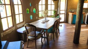 A dining area with a wooden table and chairs, large windows, and a plant on the table. - Ecological mud house (Maldonado)