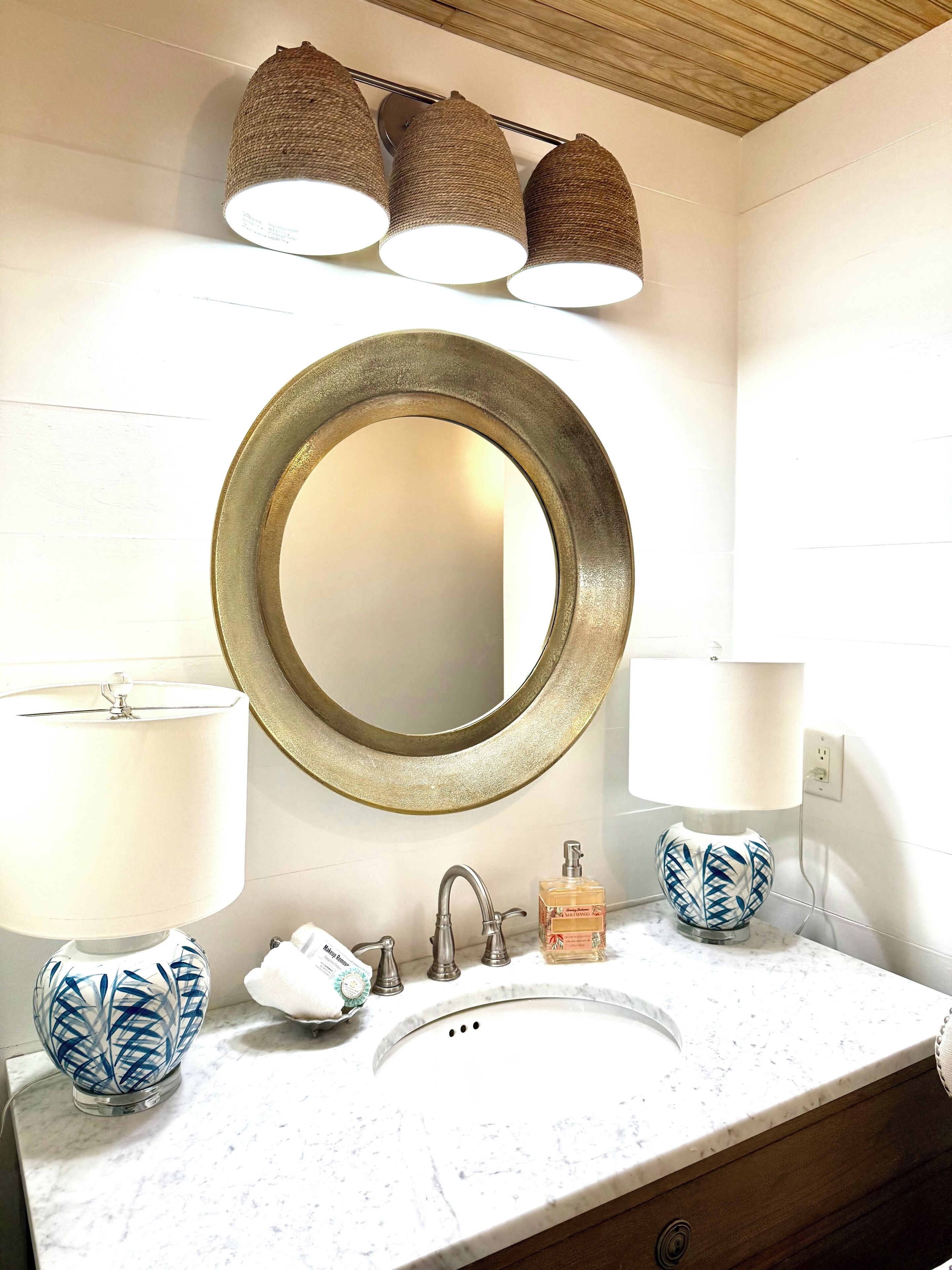 Une salle de bain avec un miroir rond, un lavabo et trois lampes suspendues.