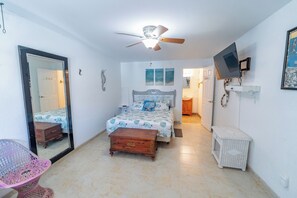 Une chambre à coucher comprenant un lit, un ventilateur de plafond, un téléviseur et une porte donnant sur une autre pièce.