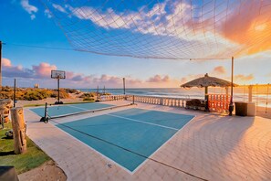 Een tennisbaan buiten met een net, een basketbalring en uitzicht op het strand.