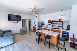 Een moderne keuken met een centraal eiland, barkrukken, een plafondventilator en een flatscreen televisie aan de muur.