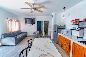 Ein zeitgemäßer Wohnraum mit Sofa, Esstisch, Küchenzeile und Deckenventilator.