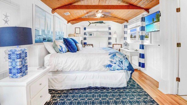 Una camera da letto con soffitto in legno, un letto con biancheria azzurra e bianca, un comodino con una lampada e un televisore a parete.