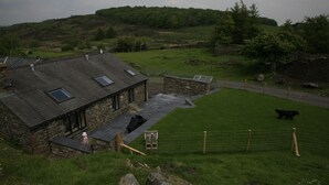 Una casa de piedra con techo inclinado, un patio cercado y un oso a lo lejos.