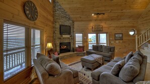 L’intérieur chaleureux d’un chalet en bois, avec une cheminée en pierre, un plafond en bois et un coin salon confortable.