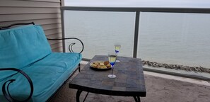 Ein Balkon mit einem blauen Sofa und einem Tisch mit einem Weinglas und Snacks.