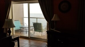 Ein Zimmer mit Meerblick durch eine Schiebetür, ein Sessel, ein Tisch und eine Lampe.